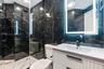 Bathroom featuring full-height dark stone tile walls, white vanity with integrated basin, matte black fixtures, glass-enclosed shower, and a back-lit 
