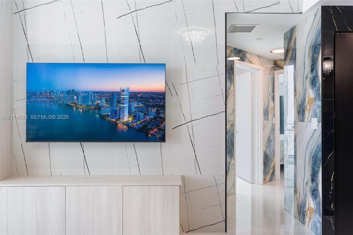 Living area featuring large-format veined stone wall cladding, built-in floor-to-ceiling cabinetry, polished tile flooring, and a kitchen island with 