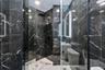 Walk-in shower featuring dark veined stone-finish tile surround, glass enclosure, square rainfall shower head, integrated LED-lit vanity mirror, and w