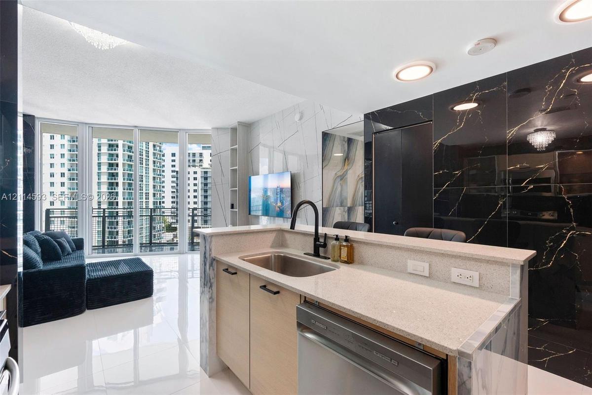 Kitchen featuring a light-toned cabinetry peninsula with stone-finish countertops, stainless steel sink with matte black faucet, and polished large-fo