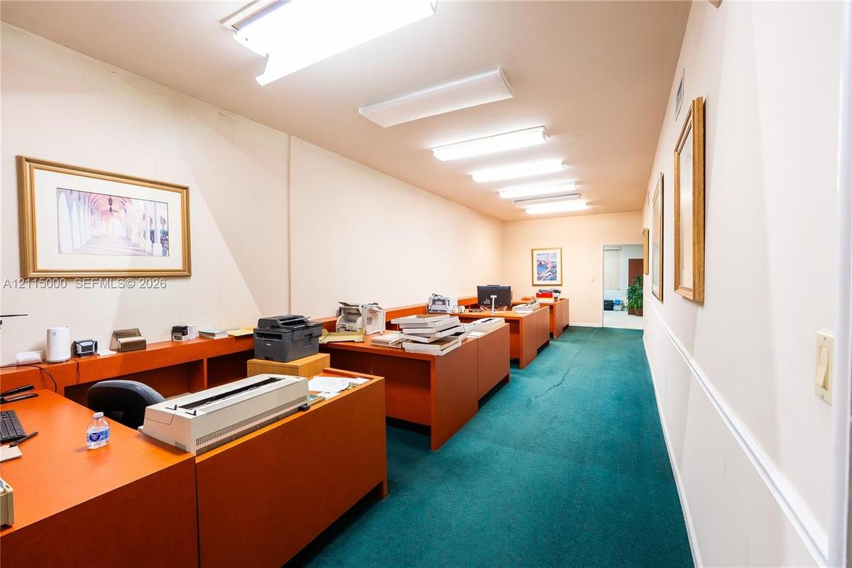 Interior workspace featuring linear fluorescent overhead lighting and fixed wooden-finish cabinetry with integrated desk surfaces