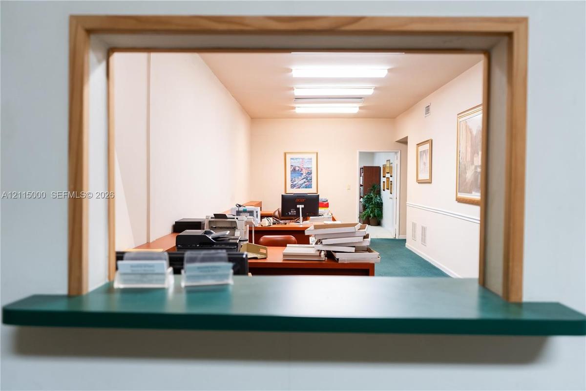 Built-in laminate desk stations, wall-to-wall carpeting, multiple linear ceiling-mounted light fixtures, and neutral wall finishes