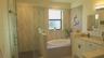Bathroom featuring a glass-enclosed walk-in shower with textured wall tile, a deep soaking tub with geometric tile surround, white cabinetry, and a va
