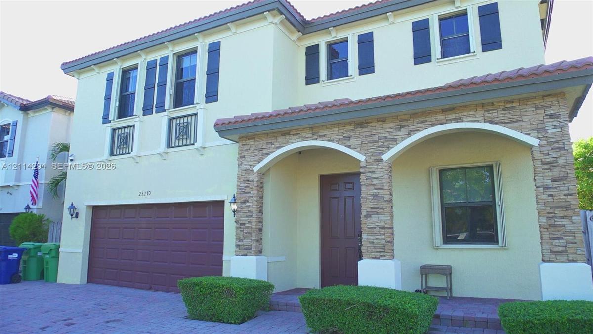 Two-story exterior featuring a stone-veneer facade, arched entryway, brick-paver driveway, decorative window shutters, and a multi-car garage