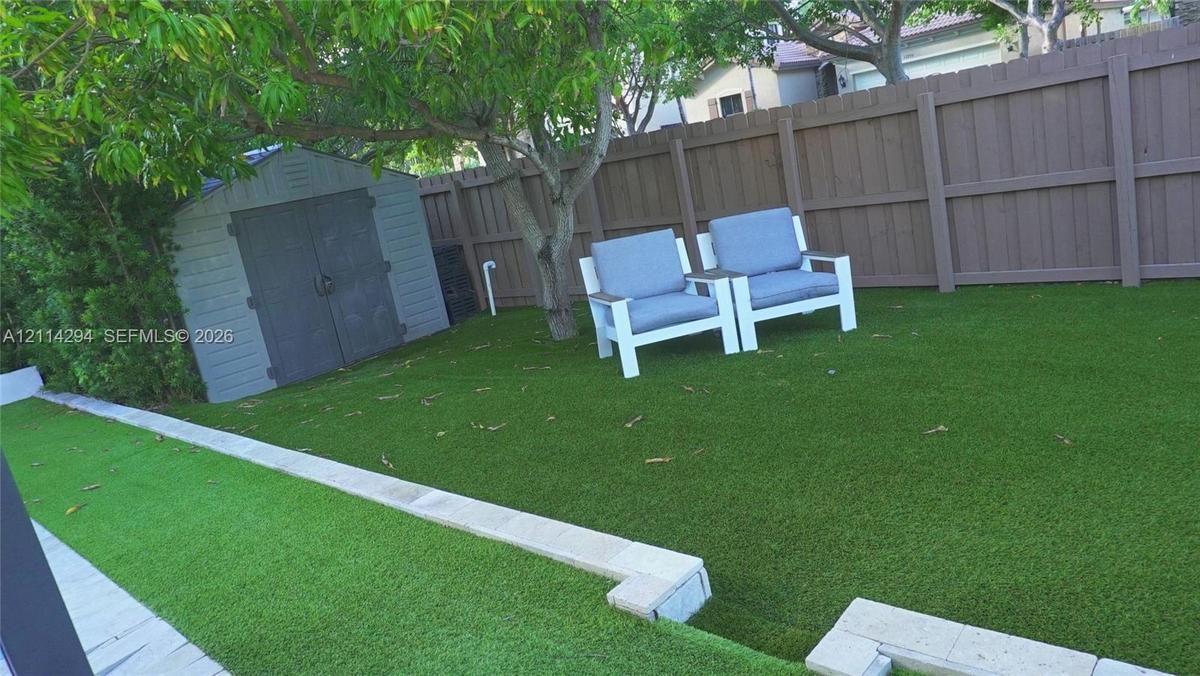 Backyard featuring synthetic turf, tiered stone-block retaining walls, a grey storage shed, and a solid-panel privacy fence