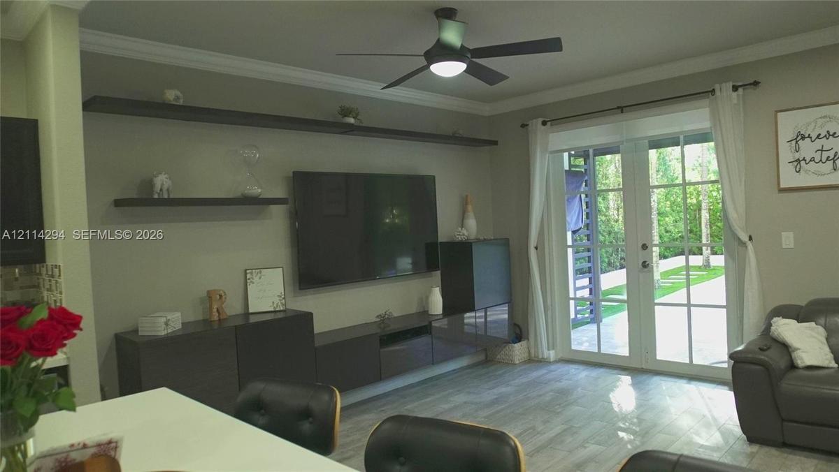 Living area featuring multi-panel glass French doors, wood-finish flooring, crown molding, built-in dark cabinetry with floating shelving, and a moder