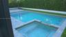 Backyard featuring an in-ground swimming pool, attached spa, stone paver decking, and perimeter privacy hedging