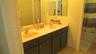 Dual-sink vanity featuring a solid surface countertop, dark-finish cabinetry, chrome-finish faucets, and an expansive wall-mounted mirror