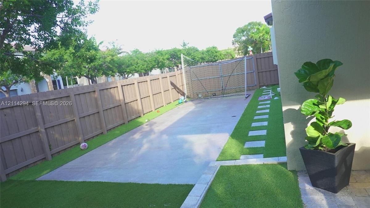 Fenced backyard featuring a concrete patio, synthetic turf lawn, and stone paver walkway