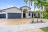 Single-story residence featuring a paver driveway, arched entryway, multi-panel garage door, and mature landscaping