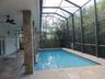 Screen-enclosed pool area featuring stone-tile decking, stone-clad structural pillars, recessed ceiling fans, and an attached covered patio