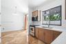 Kitchen featuring stone tile flooring, flat-panel wood cabinetry, quartz countertops, stainless steel appliances, and a stainless steel undermount sin