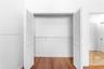 Storage area featuring dual white louvered bi-fold doors, wood-finish flooring, and integrated wire shelving