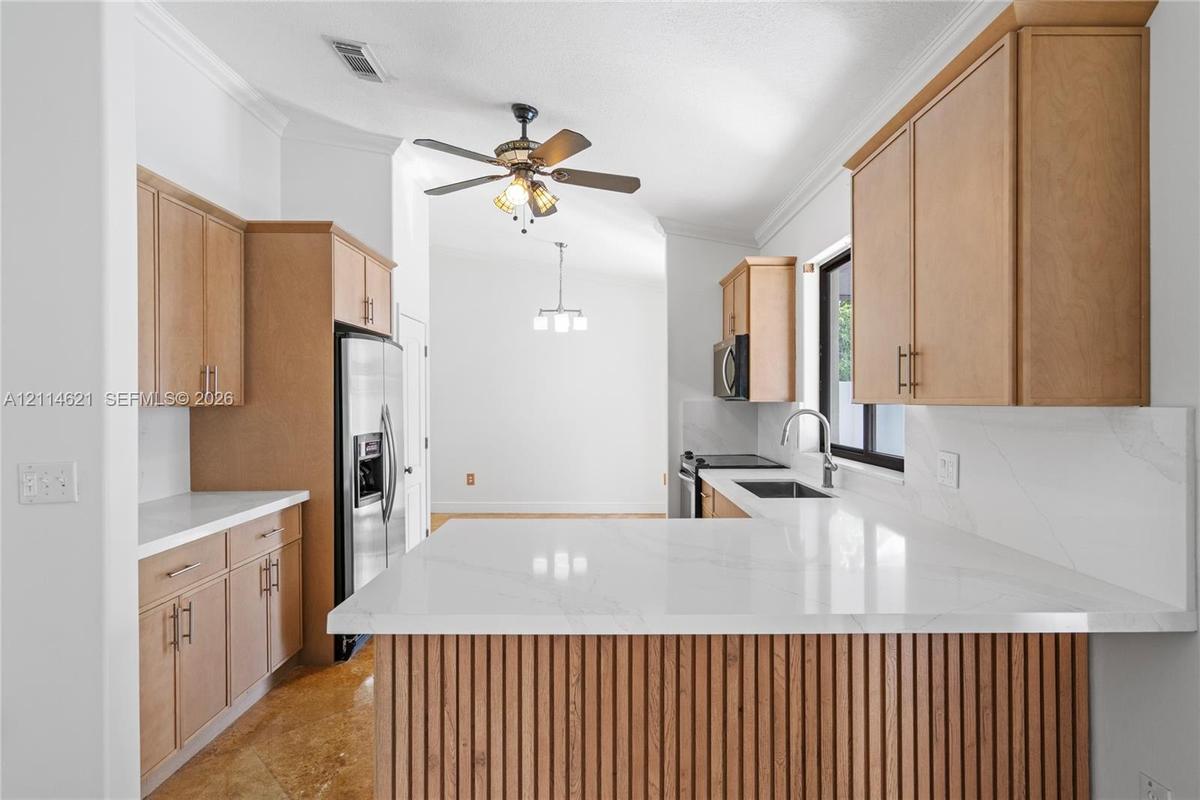 Kitchen featuring flat-panel wood cabinetry, white stone-finish countertops, slatted wood kitchen island detailing, stainless steel appliances, and a 
