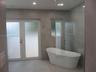 Freestanding soaking tub with a floor-mounted faucet, large-format grey tile wall cladding, glass shower enclosure, and white frosted glass double doo