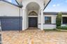 Exterior facade featuring a herringbone-patterned paver driveway, arched entryway with dual columns, double front doors with a semi-circular transom w
