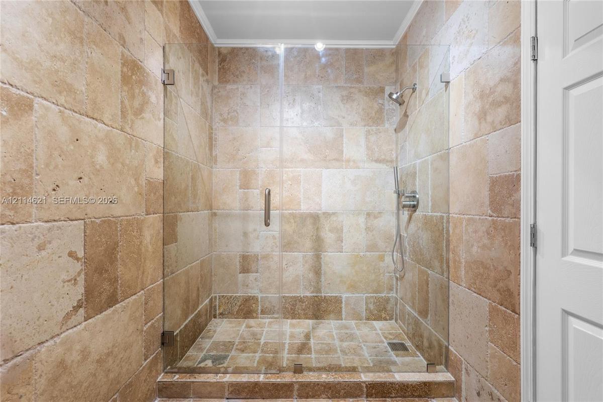 Walk-in shower featuring natural stone tile surround, frameless glass door, handheld shower head, and recessed ceiling lighting