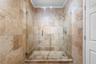 Walk-in shower featuring natural stone tile surround, frameless glass door, handheld shower head, and recessed ceiling lighting