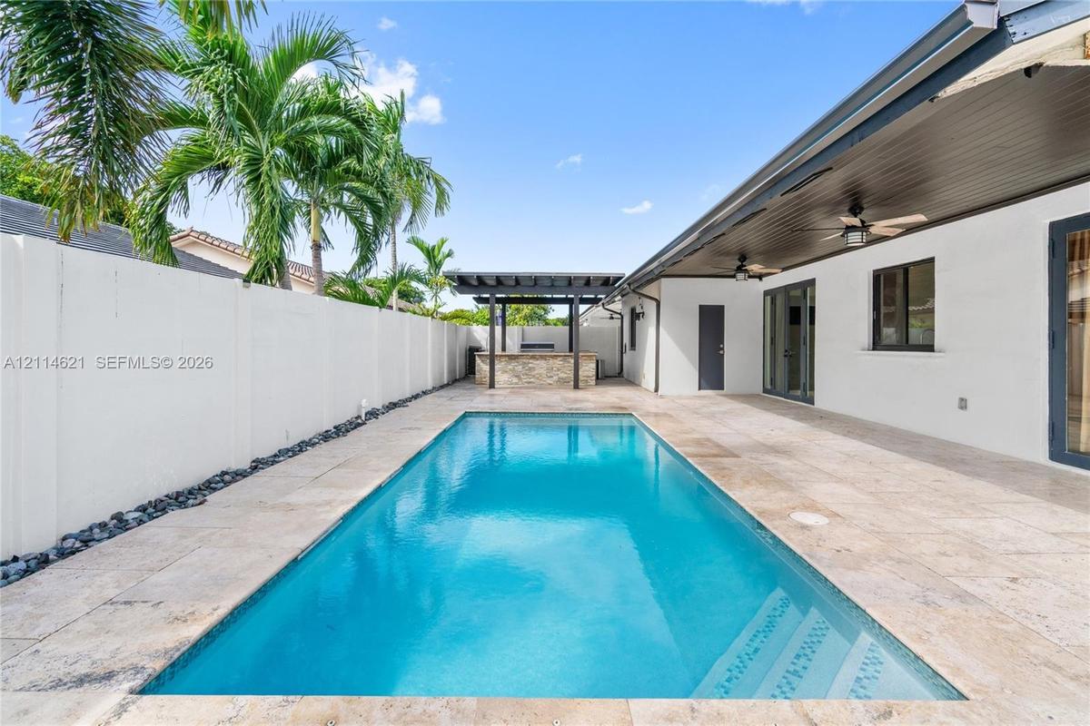 Outdoor space featuring a rectangular swimming pool, stone-tiled patio, built-in outdoor bar with a pergola, covered lanai with ceiling fans, and a so