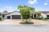 Single-story exterior featuring a light-toned stucco façade, a multi-car garage with a paneled door, a paved driveway, a tile roof, and curated tropic