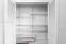 Storage closet featuring white louvered bifold doors, adjustable shelving tracks, and multiple solid surface shelves