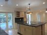 Kitchen featuring an expansive center island with a built-in cooktop, stone-finish countertops, custom wood cabinetry with integrated wine storage, an