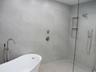 Freestanding soaking tub with floor-mounted faucet, walk-in shower featuring large-format tile surround, integrated tiled wall niche, rain shower head