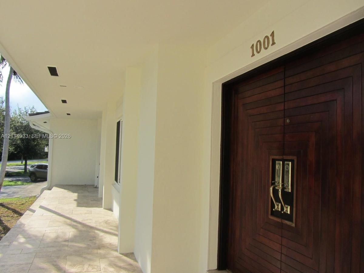 Covered entryway featuring natural stone tile flooring, recessed ceiling lighting, and double doors with dark wood finish and geometric relief detail