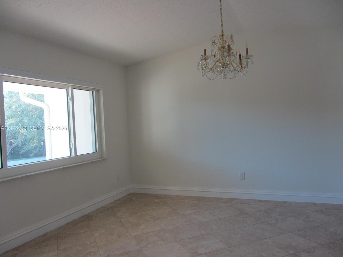 Vaulted ceiling, multi-light crystal chandelier, large-format tile flooring, and a wide horizontal window