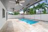 Covered patio featuring a grey tongue-and-groove ceiling with dual ceiling fans, stone paver decking, and a rectangular swimming pool enclosed by a wh