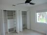 Dual closets with built-in shelving and integrated drawer storage, neutral tile flooring, and a ceiling fan with integrated light fixture
