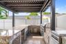 Outdoor kitchen featuring a stone-clad base, built-in stainless steel grill, stone countertop, undermount sink, and overhead pergola