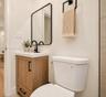Wood-finish vanity with a rectangular sink, matte black faucet, rounded rectangular mirror, and matte black towel hardware