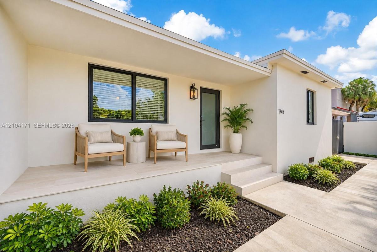 Stucco exterior featuring an expansive covered porch, tiled flooring, dark-framed windows, and a glass-panel entry door