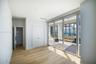 Minimalist interior featuring wood-finish flooring, floor-to-ceiling windows, and high-rise water and cityscape backdrops