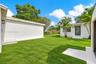 Backyard featuring a manicured lawn, perimeter masonry wall, detached storage structure, concrete walkway, and exterior wall-mounted lighting
