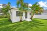 Stucco exterior featuring black-framed windows, a glass-panel entry door, concrete steps, and mature palm trees situated on a grassy lot enclosed by a