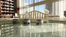 Floor-to-ceiling glass windows, wood-finish flooring, recessed lighting, and balcony access with water and city skyline surroundings