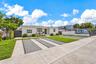 Single-story residence featuring a light-toned stucco exterior, multi-vehicle concrete parking area with permeable pavers, front covered entryway, and