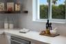 Kitchen featuring light-toned solid surface countertops, white subway tile backsplash, stainless steel dishwasher, and floating wood-finish shelving
