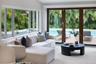 Expansive multi-pane windows and large-format sliding glass doors with dark wood frames, offering visibility to the outdoor pool and lush foliage