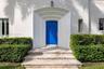 Stucco exterior entrance featuring an arched recessed doorway, paneled front door, stone steps, and manicured shrubbery