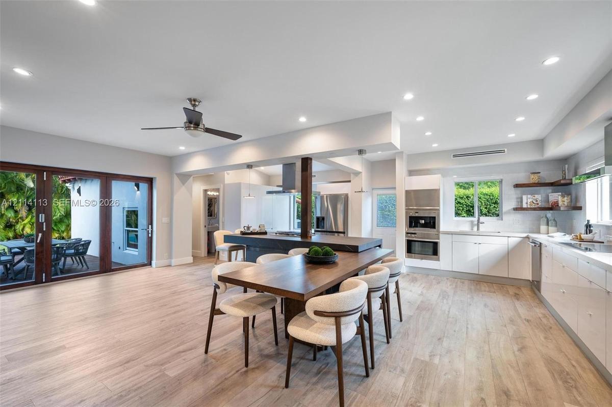 Open-concept kitchen, white cabinetry, recessed lighting, stainless steel wall ovens, and multi-panel glass doors