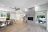 Light-toned wood-finish flooring, central fireplace with a grey smooth-finish surround, recessed ceiling lighting, ceiling fans, and multi-paned windo