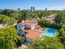 Two-story residence featuring a terracotta-tiled roof, rectangular swimming pool, wood-decking patio, and manicured landscaping