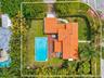 Aerial perspective of a corner lot property featuring a barrel tile roof, an in-ground swimming pool, wood-finish decking, and perimeter privacy hedgi