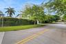 View of the side W 54th street featuring a tall perimeter privacy hedge, manicured lawn, and mature trees