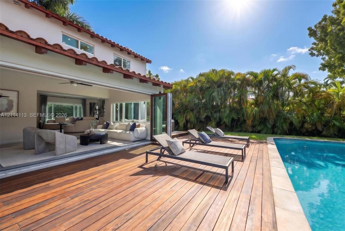 Outdoor space featuring a wood-plank deck, built-in swimming pool, terracotta-tiled roofline, and multi-panel folding glass doors