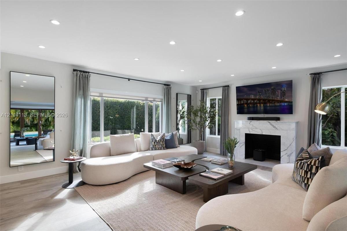Spacious interior filled with natural light, featuring recessed lighting, stone-finish fireplace surround, large-format windows, and wood-finish porce