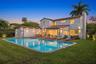 Two-story stucco exterior with a clay tile roof, oversized swimming pool, wood-finish decking, and multi-panel folding glass doors